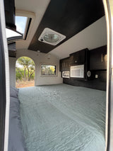 Inside a comfy RV rental bedroom featuring a spacious bed, AC units, and scenic outdoor views.