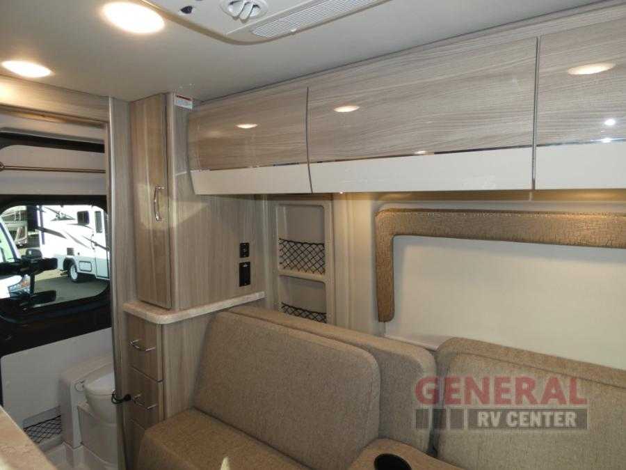 Bright RV rental interior showing light woodgrain cabinets, comfortable seating, and a compact bathroom. — photo 7