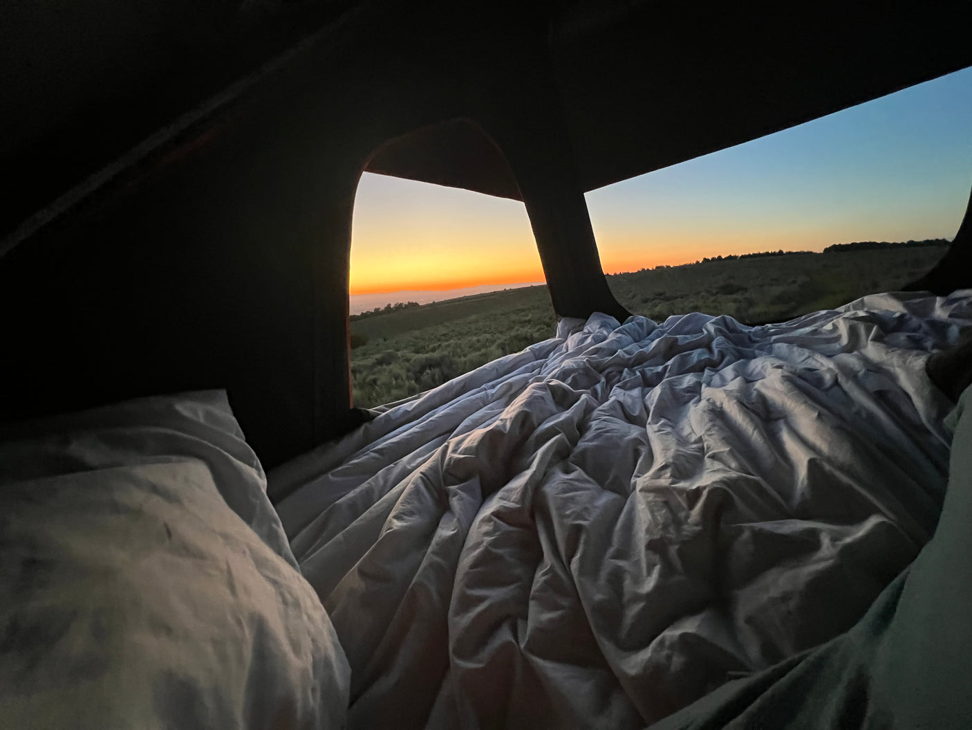 Waking to a serene sunrise from a cozy, unmade bed inside an rv rental. Rolling green hills in view.