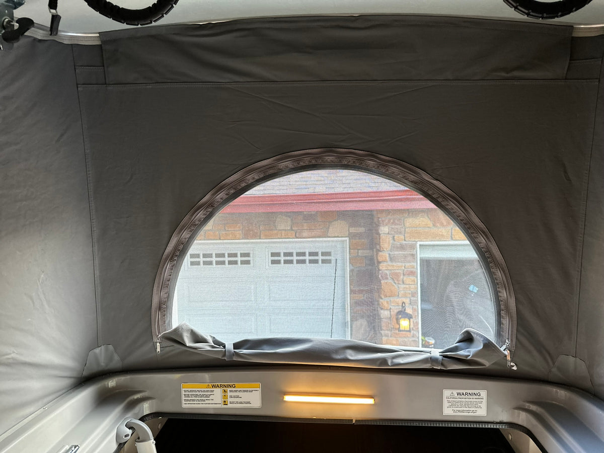 RV rental pop-up roof interior, gray fabric, with a semi-circular screen window tied open, revealing a garage outside. — photo 18