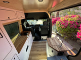 Spacious RV rental interior featuring a modern kitchen, wooden accents, and an open door view of lush plants outside. Perfect for van life!