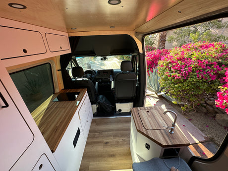 Spacious RV rental interior featuring a modern kitchen, wooden accents, and an open door view of lush plants outside. Perfect for van life!