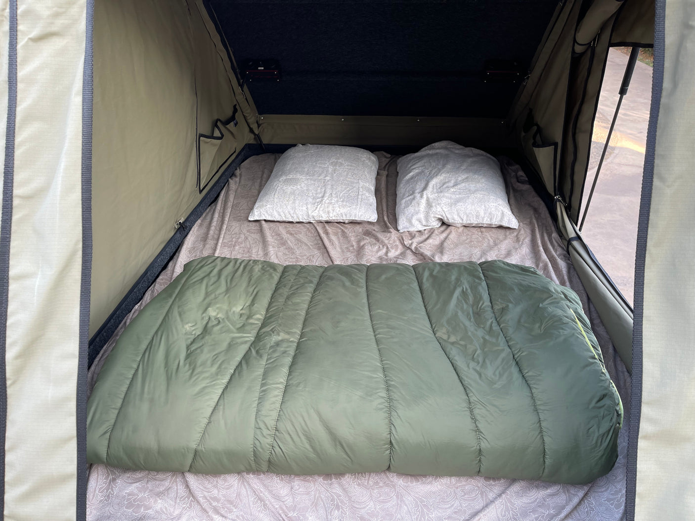 Cozy rv rental rooftop tent interior features a bed with two pillows and a green sleeping bag, ready for adventure.