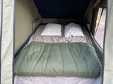 Cozy rv rental rooftop tent interior features a bed with two pillows and a green sleeping bag, ready for adventure.