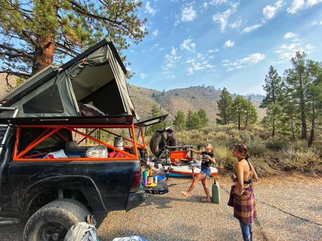Truck with rooftop tent for camping. Cooking outdoors, an alternative to RV rental, amidst hills and pines.