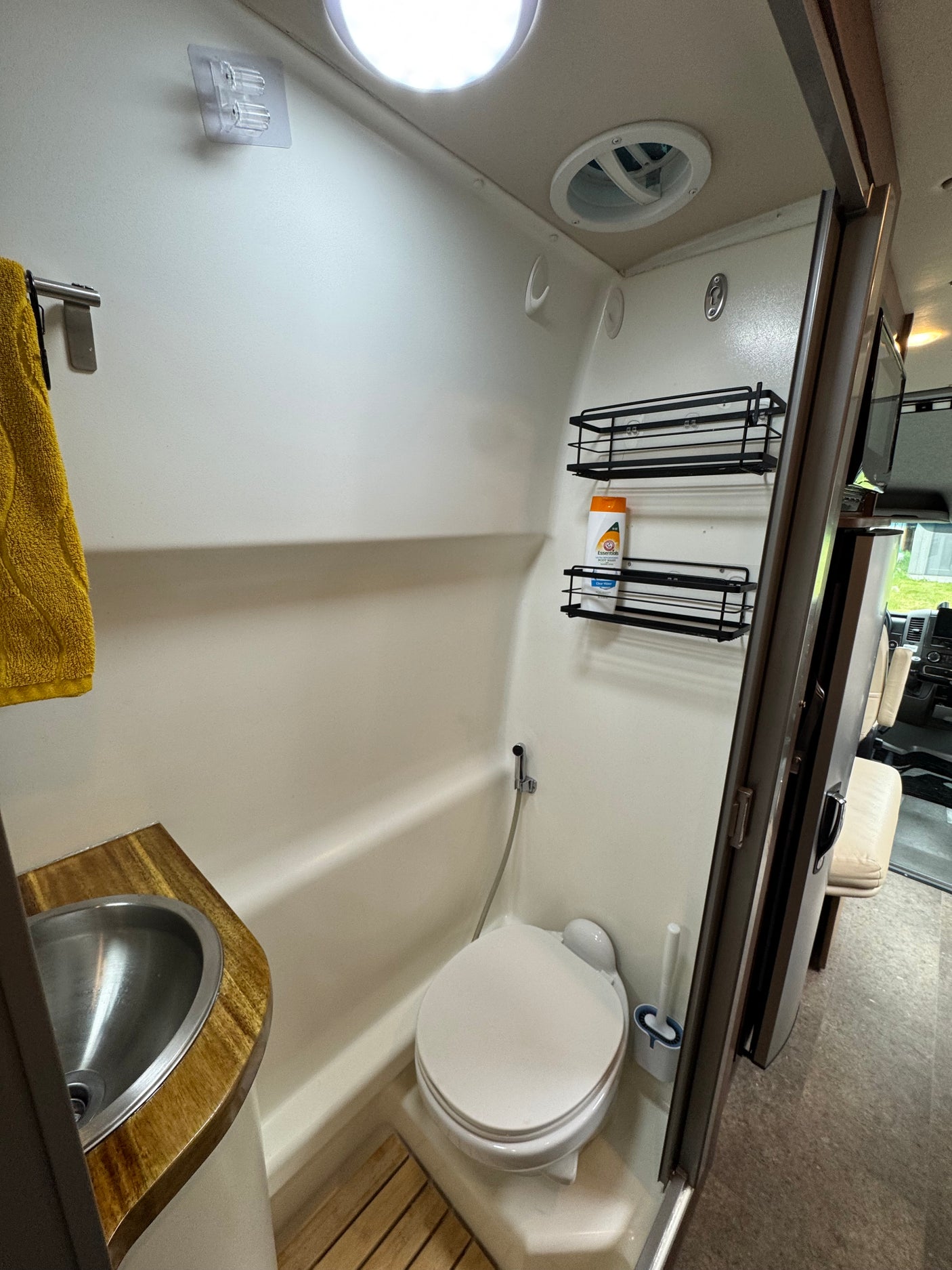 Compact RV rental bathroom featuring a toilet, sink with wooden counter, and shower, with toiletries and hooks on the wall.