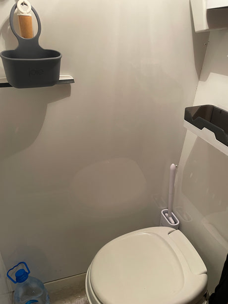 Compact RV rental bathroom features a white toilet, brush, water bottle, and wall-mounted storage solutions.