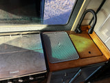 RV rental galley showing stove, sink with wooden cover, flexible faucet, OXO drainer, and outdoor window view.