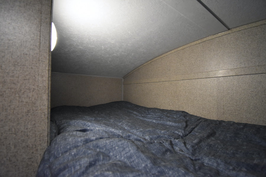 Cozy RV rental bunk with a blue comforter, lit by a side lamp under a curved ceiling. — photo 16