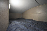 Cozy RV rental bunk with a blue comforter, lit by a side lamp under a curved ceiling.
