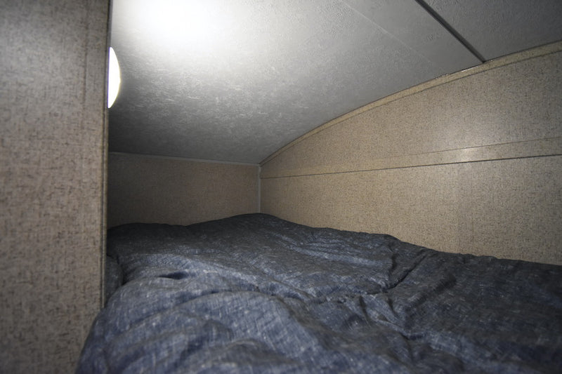 Cozy RV rental bunk with a blue comforter, lit by a side lamp under a curved ceiling. — photo 16