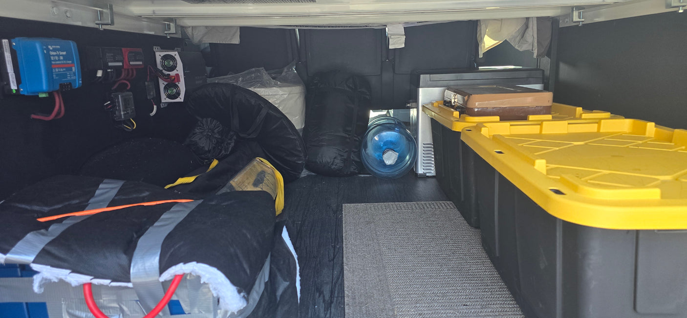 Inside an RV rental's gear storage: custom power electronics, water jug, portable cooler, and stackable storage bins.