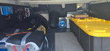 Inside an RV rental's gear storage: custom power electronics, water jug, portable cooler, and stackable storage bins.