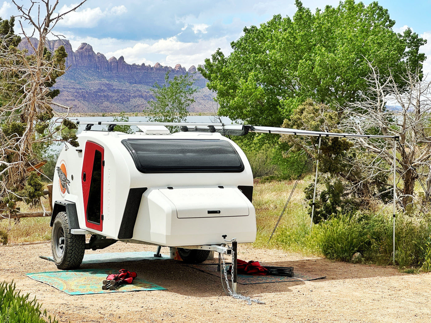 This white teardrop RV rental sits by a lake, offering mountain views and a cozy camp setup with an awning. — photo 13