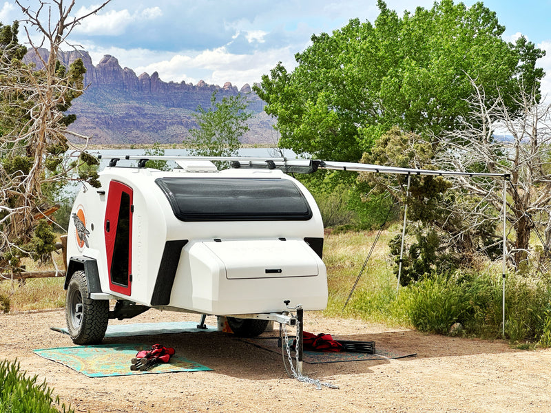 This white teardrop RV rental sits by a lake, offering mountain views and a cozy camp setup with an awning. — photo 13