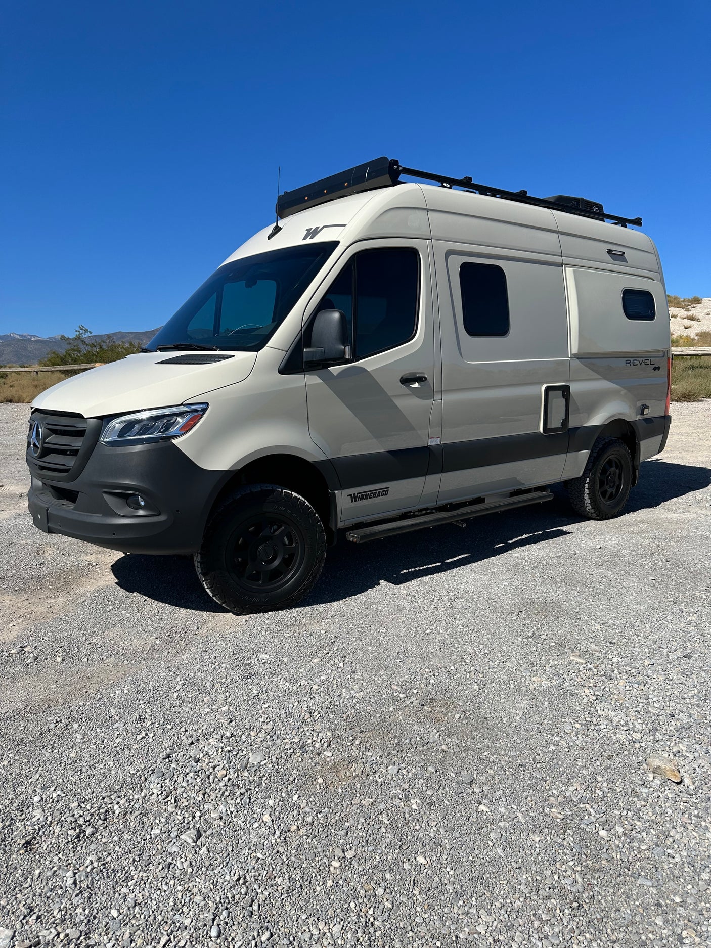 Winnebago Revel camper van, ideal rv rental for adventure, parked on gravel under a clear sky.