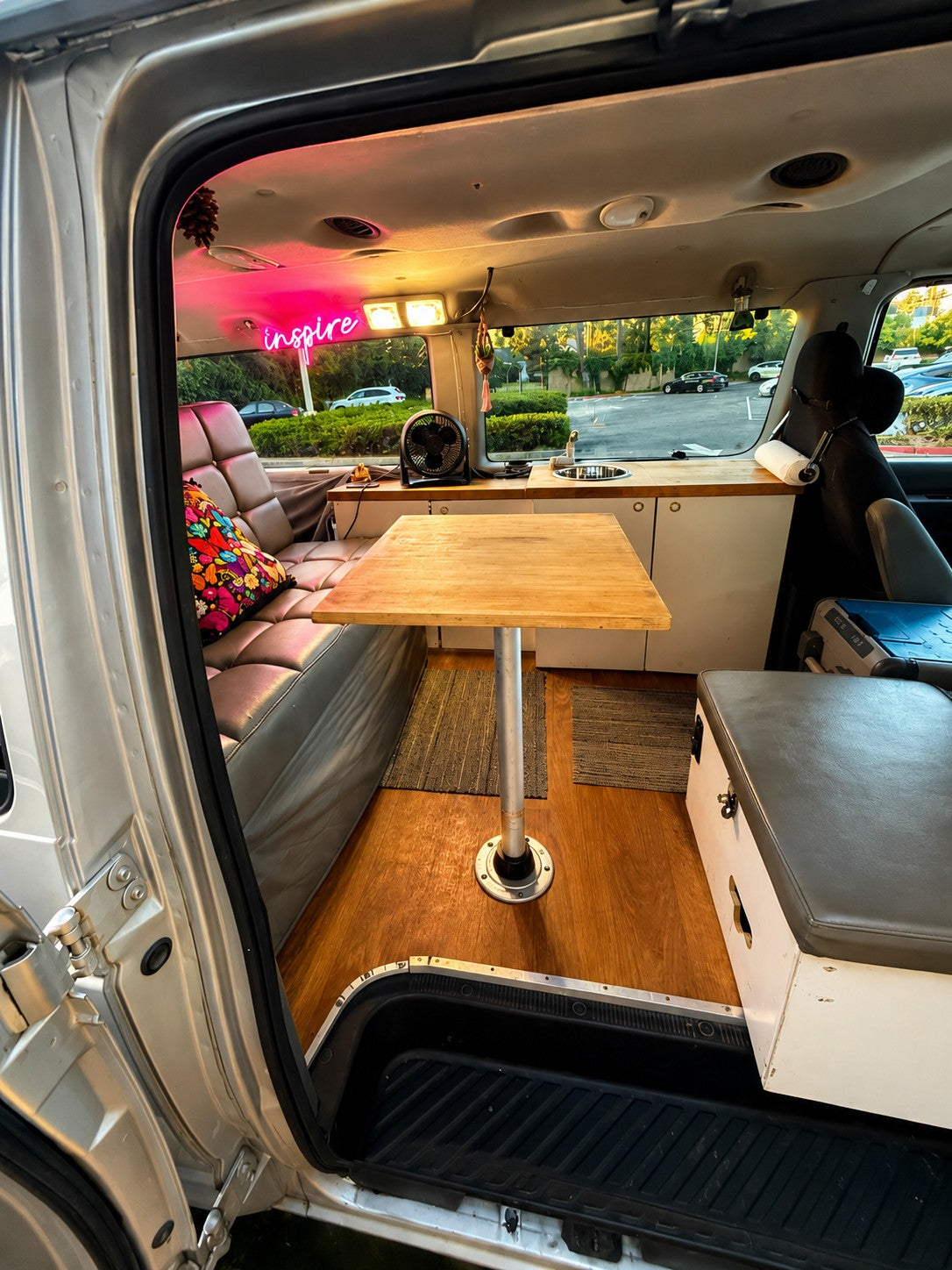 Cozy rv rental interior featuring a dining area, small kitchen, and a pink "inspire" neon sign, viewed from the open side door.