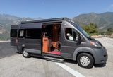 Gray RV rental parked by mountains, with its side & back doors open, revealing interior and two dogs.