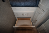 RV rental interior: Light wood cabinetry with an open storage drawer below a bed, revealing functional storage space.