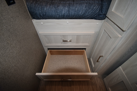 RV rental interior: Light wood cabinetry with an open storage drawer below a bed, revealing functional storage space.
