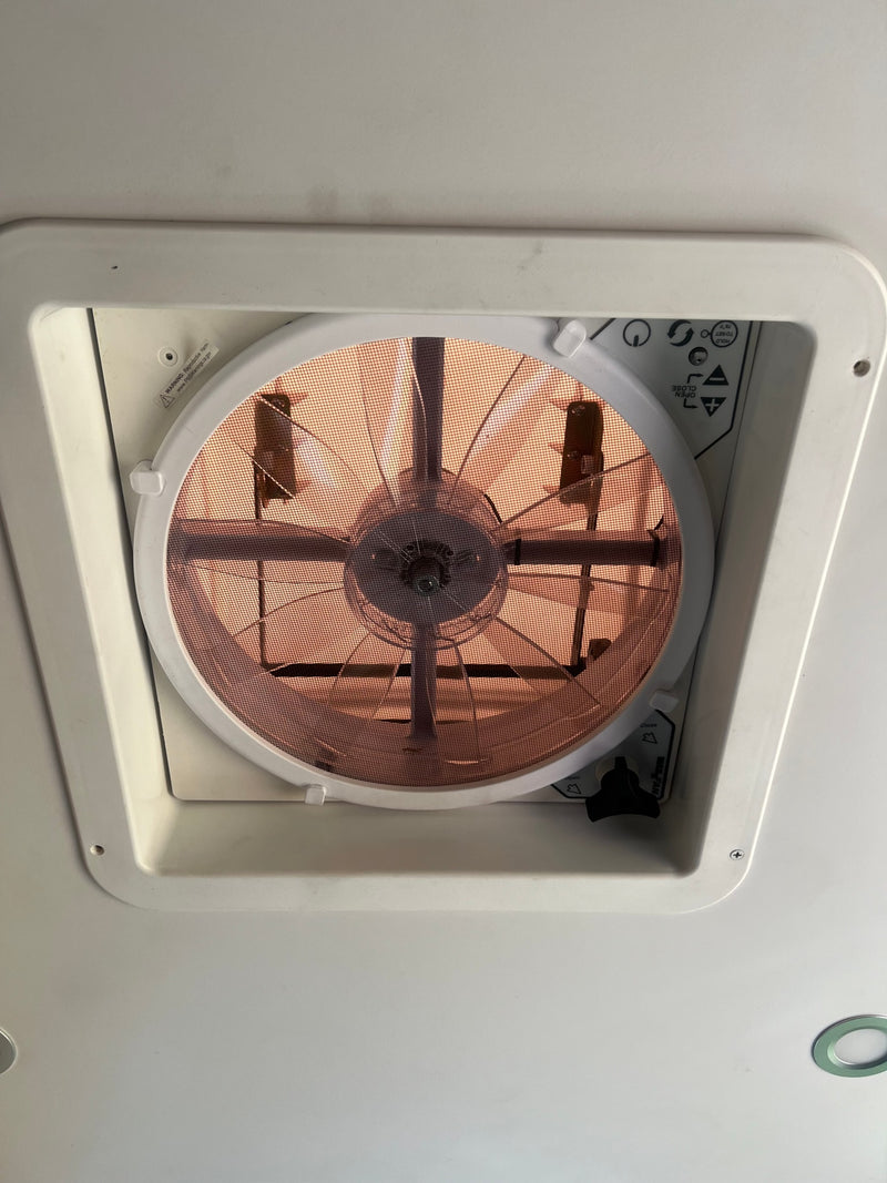 Overhead view of an RV rental ceiling vent fan, displaying its protective mesh, fan blades, and function controls. — photo 16