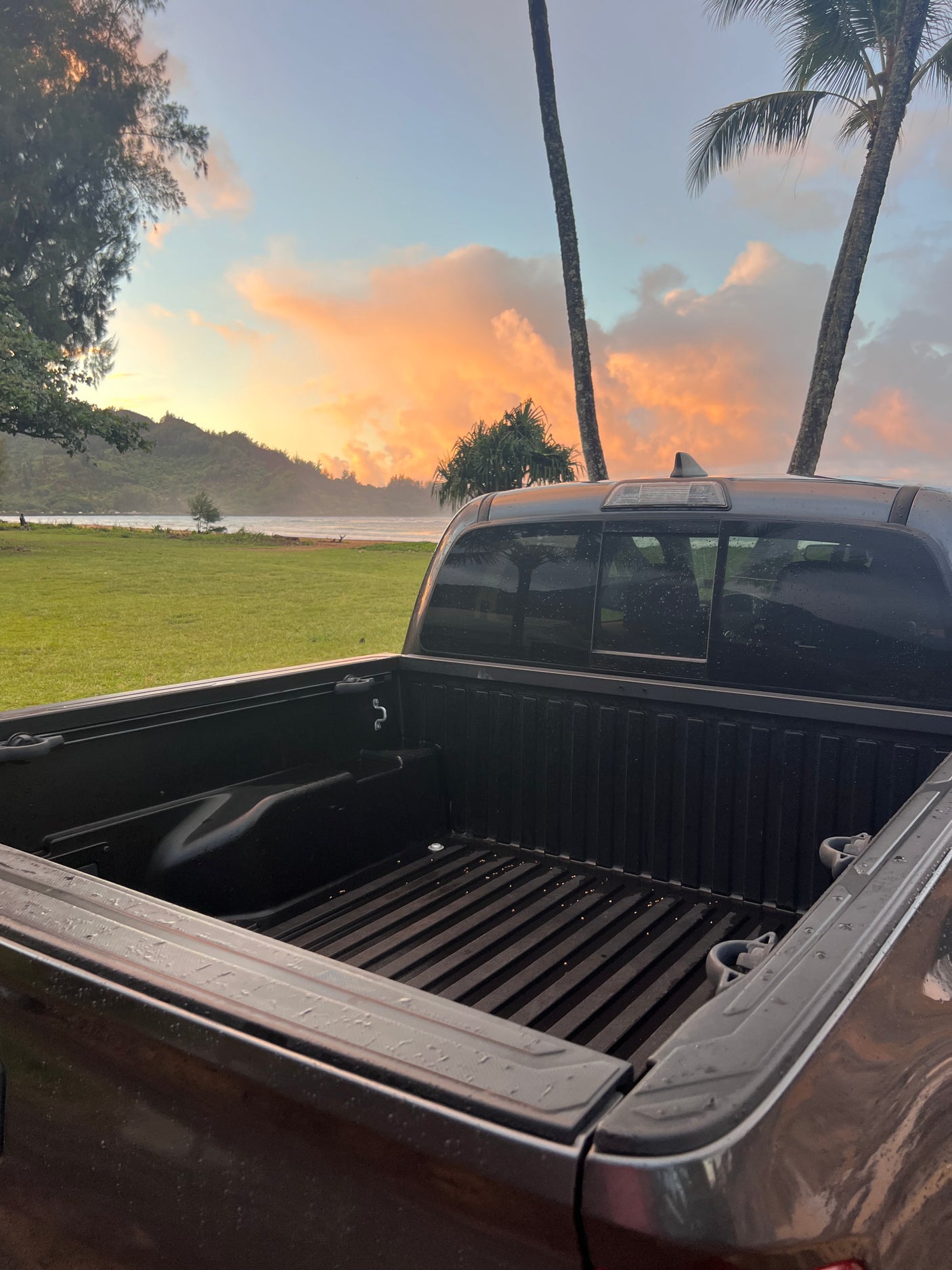 Wet truck bed faces a stunning tropical sunset/sunrise over a bay. Perfect for gearing up for an RV rental adventure!