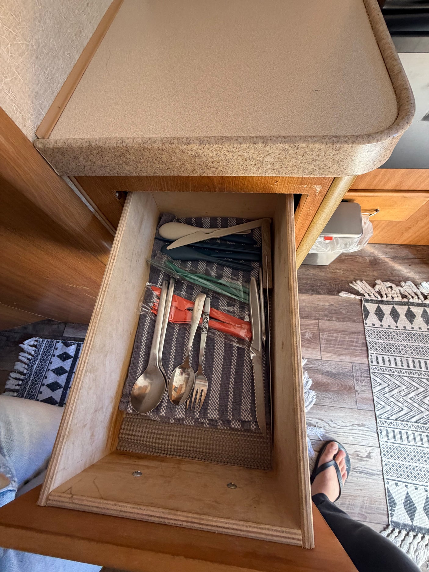 Open drawer in an rv rental, neatly organizing metal and plastic cutlery on a striped cloth, showcasing essential kitchen storage.