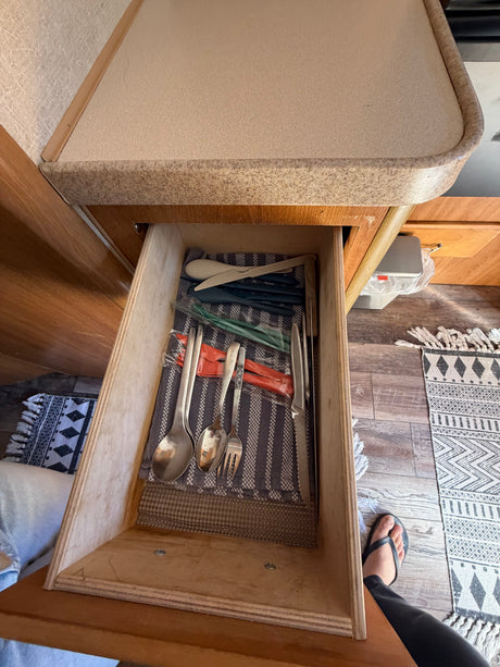Open drawer in an rv rental, neatly organizing metal and plastic cutlery on a striped cloth, showcasing essential kitchen storage.