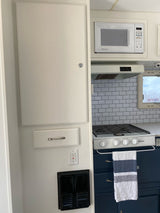 Compact RV rental kitchen featuring a Dometic microwave, Suburban stove, subway tile, and modern blue cabinets.