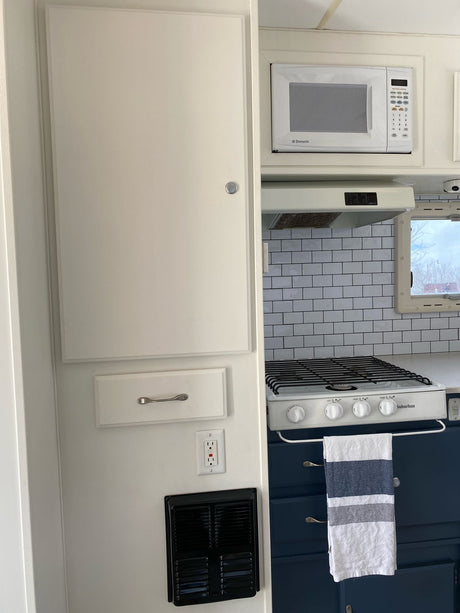 Compact RV rental kitchen featuring a Dometic microwave, Suburban stove, subway tile, and modern blue cabinets.