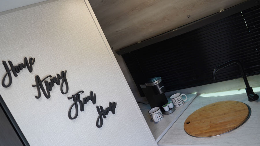 Enjoy an RV rental: Kitchenette featuring Keurig, sink with cutting board, and 'Home Away Home' wall decor.