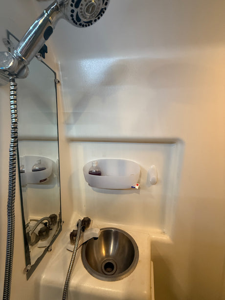 RV rental compact wet bath: chrome shower, stainless steel sink, mirror, and toiletries caddy.