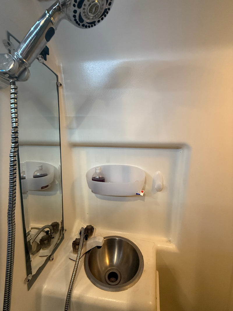 RV rental compact wet bath: chrome shower, stainless steel sink, mirror, and toiletries caddy. — photo 11