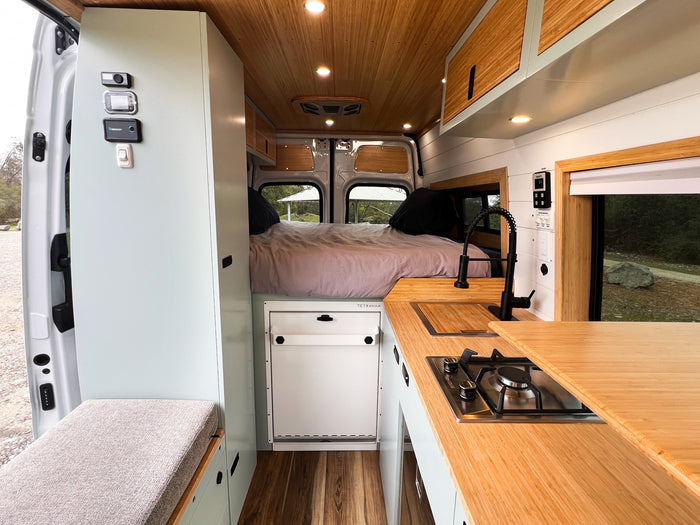 Modern RV rental camper van interior: compact kitchen, cozy bed, and stylish wood paneling.
