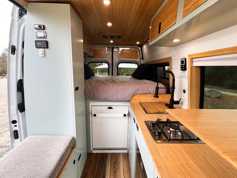 Modern RV rental camper van interior: compact kitchen, cozy bed, and stylish wood paneling.