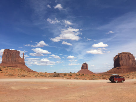 Red RV rental camper van parked in Monument Valley desert with majestic mesas under a blue sky.