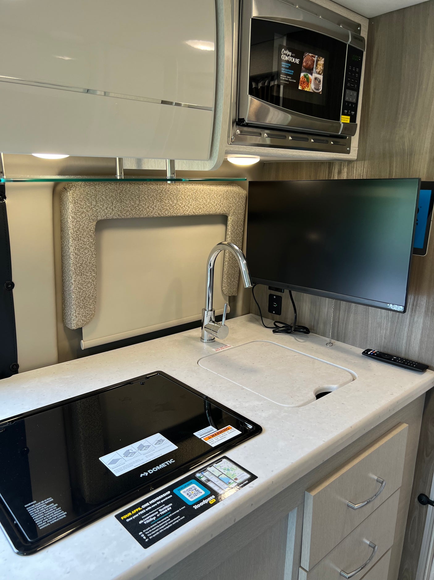 RV rental interior: A compact kitchen with a cooktop, covered sink, modern faucet, microwave, and TV.