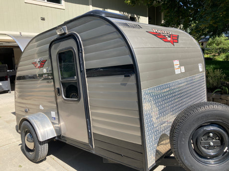 This retro teardrop camper, perfect as an RV rental, features a side door, window, and front-mounted spare tire.