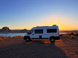RV rental parked at sunset by a lake, with rocky formations and a golden sky. Perfect for a scenic road trip.