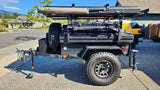 Rugged black overland trailer with rooftop tent & awning, perfect for an rv rental adventure. Includes large off-road tires & spare.