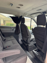 Spacious RV rental van interior with rear and front passenger seats, overhead lighting, and air vents. Curtains for privacy.