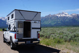 Wyoming's Grand Tetons frame this white truck camper RV rental on a dirt road. Perfect for mountain adventures.
