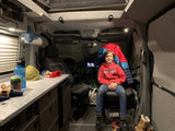 Smiling boy in an RV rental's custom camper van interior. Shows kitchen counter, front seats, & cozy living space.