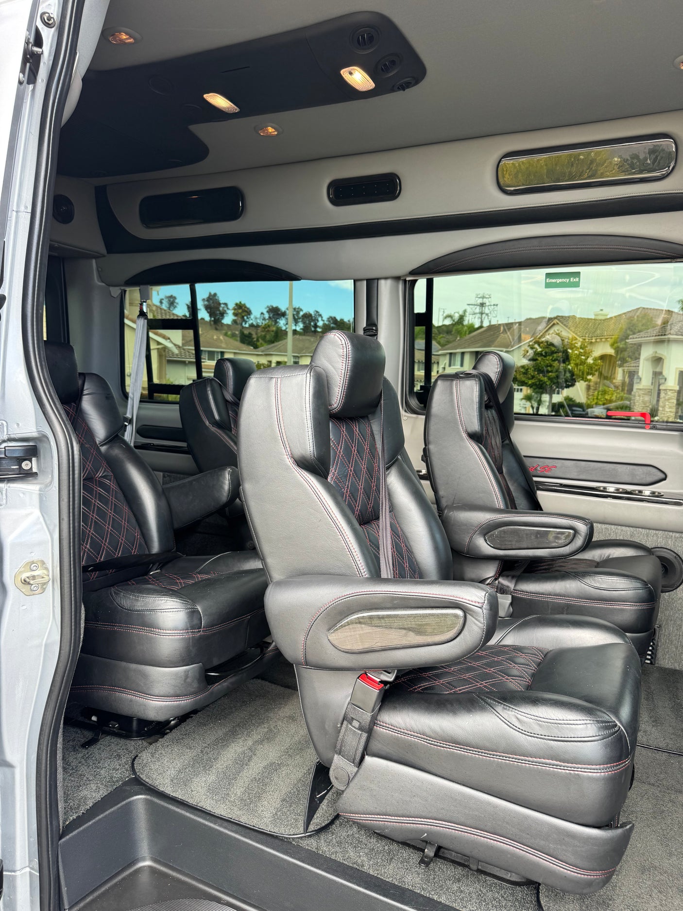 Premium RV rental van interior: black leather captain's chairs with red stitching, comfy armrests, and overhead lighting.
