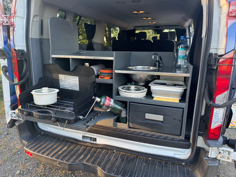 RV rental featuring a compact, pull-out kitchen setup with a camp stove, sink, and storage in the open rear of a van.