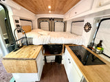 RV rental van's cozy interior: kitchen with faucet, induction cooktop, and comfortable bed for compact van life living.