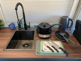 Compact RV rental kitchen features a sink, induction cooktop, kettle, knives, and cutting boards for easy meals.
