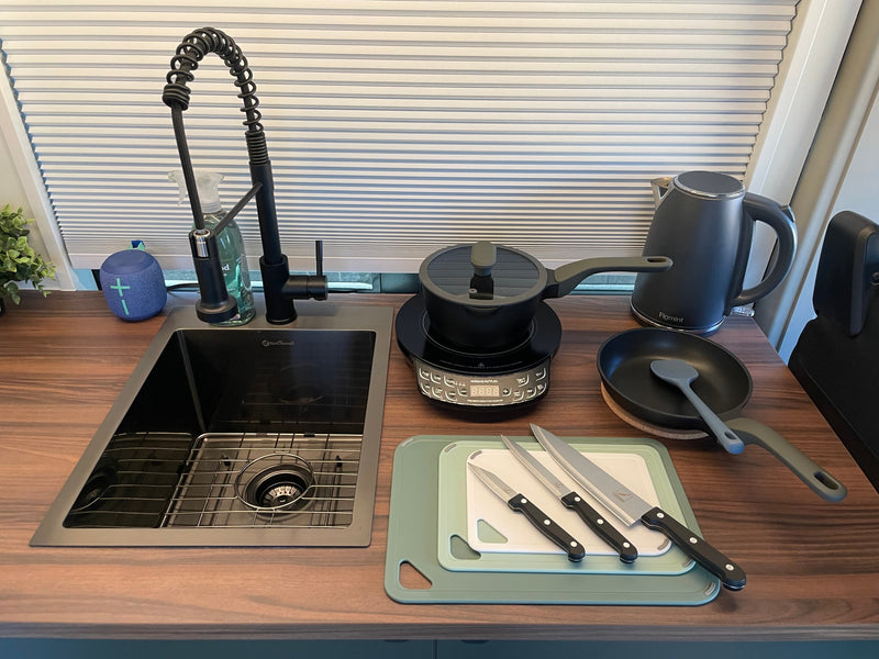 Compact RV rental kitchen features a sink, induction cooktop, kettle, knives, and cutting boards for easy meals. — photo 17