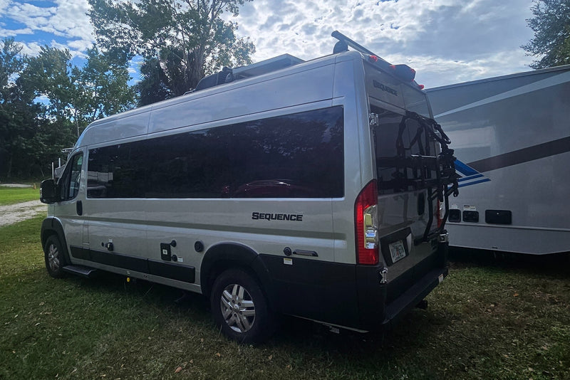  with a larger motorhome and dense trees reflecting in its windows.|A silver Thor Sequence camper van — photo 3