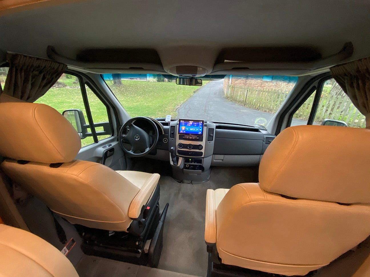 Spacious RV rental interior: tan swivel seats, dashboard with infotainment system, and steering wheel, ready for travel.